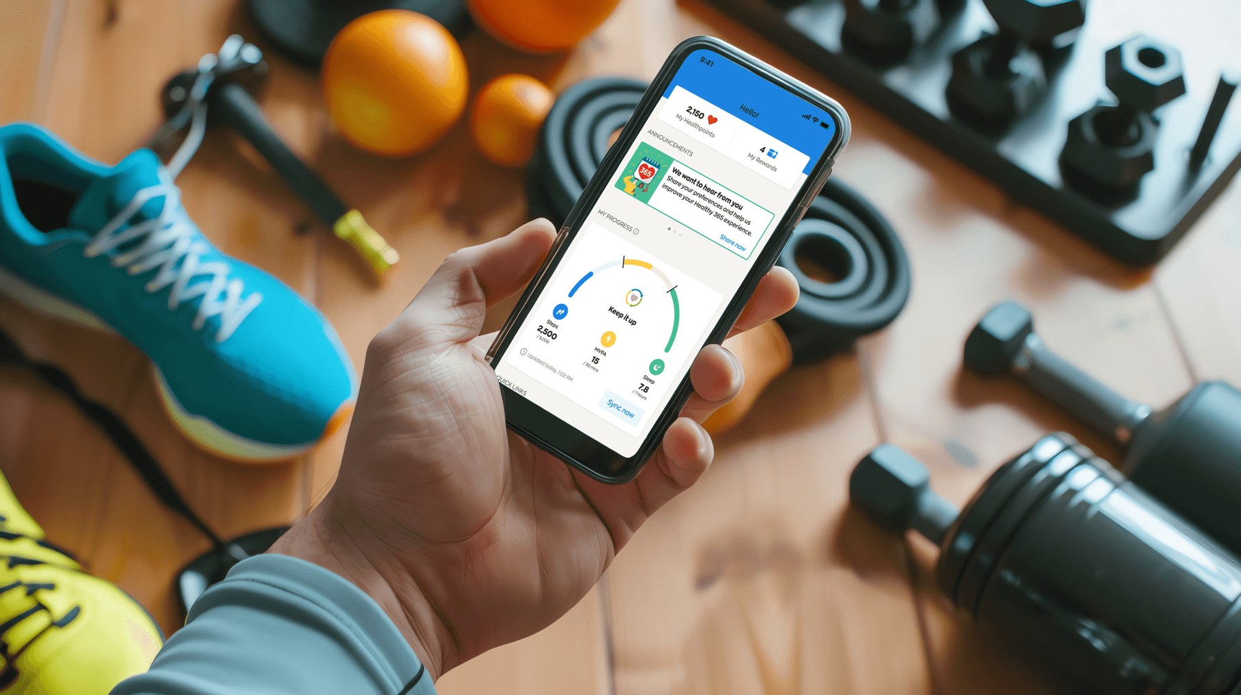 A person holding a phone showing the Healthy 365 My Progress dashboard, tracking steps, active minutes and sleep against the day's goals, amid running shoes and gym gear.